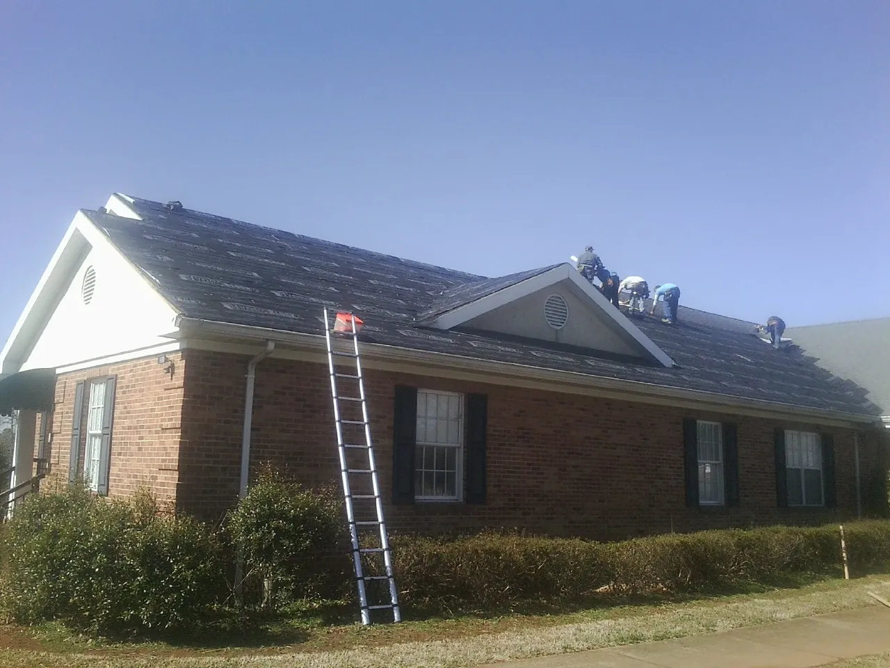 Crew tearing shingles off a brick ranch roof with a ladder set — Emergency Roof Repair work by our crew in Cochecton