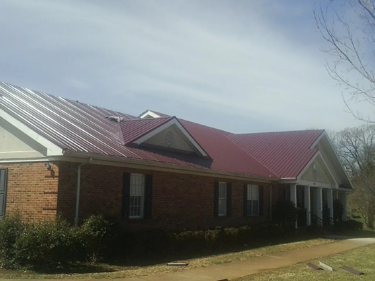 Red metal roof with gabled entries on a long brick building, from a Hail Damage Roof Repair job in Cochecton