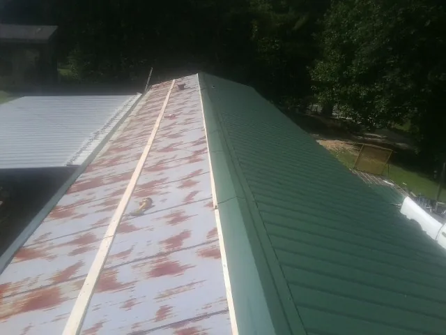 Old rusted panels beside newly installed green metal roofing — Wind Damage Roof Repair by Roofing Brothers in Cochecton