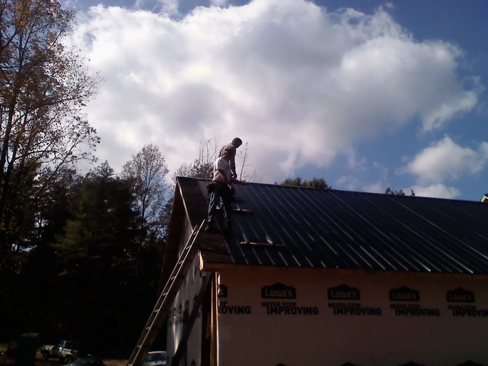 Roofer fastening dark metal panels high against a cloudy sky in Cochecton