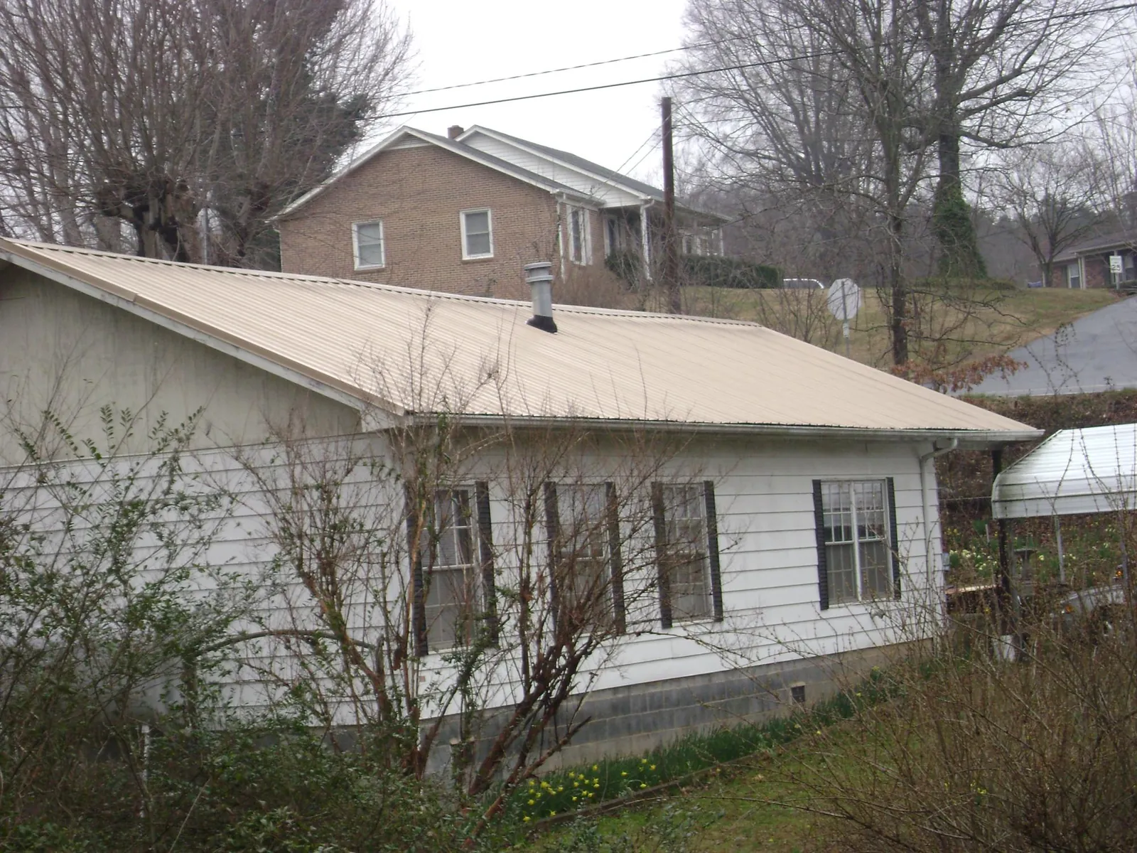 Tan metal roof on a white sided house set into a hillside — Commercial Roofing by Roofing Brothers in Cochecton